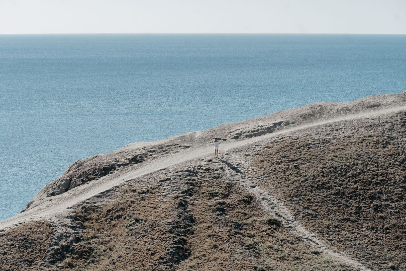Lone walker on an exposed coastal headland path above the sea