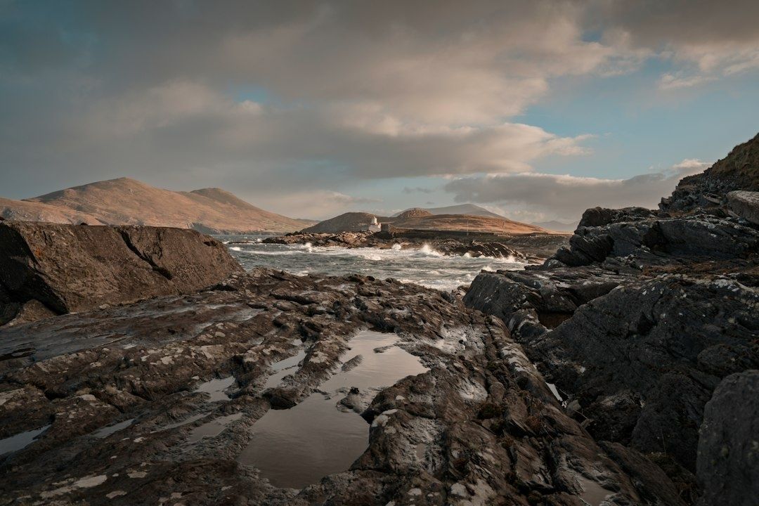 Rough Atlantic waves break between dark granite rocks beneath cloudy skies