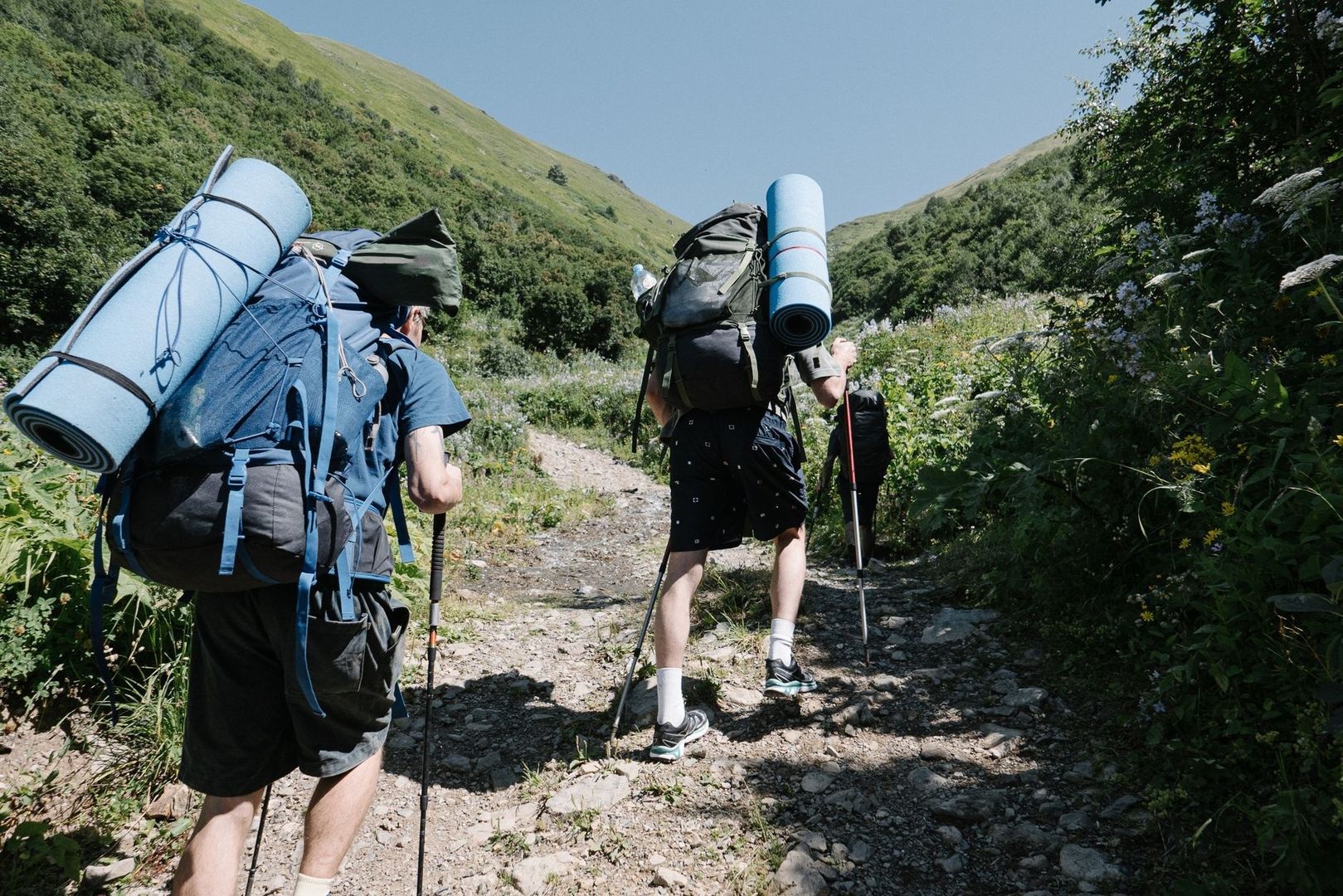 Hikers climb a steep rocky mountain trail with loaded backpacks and poles