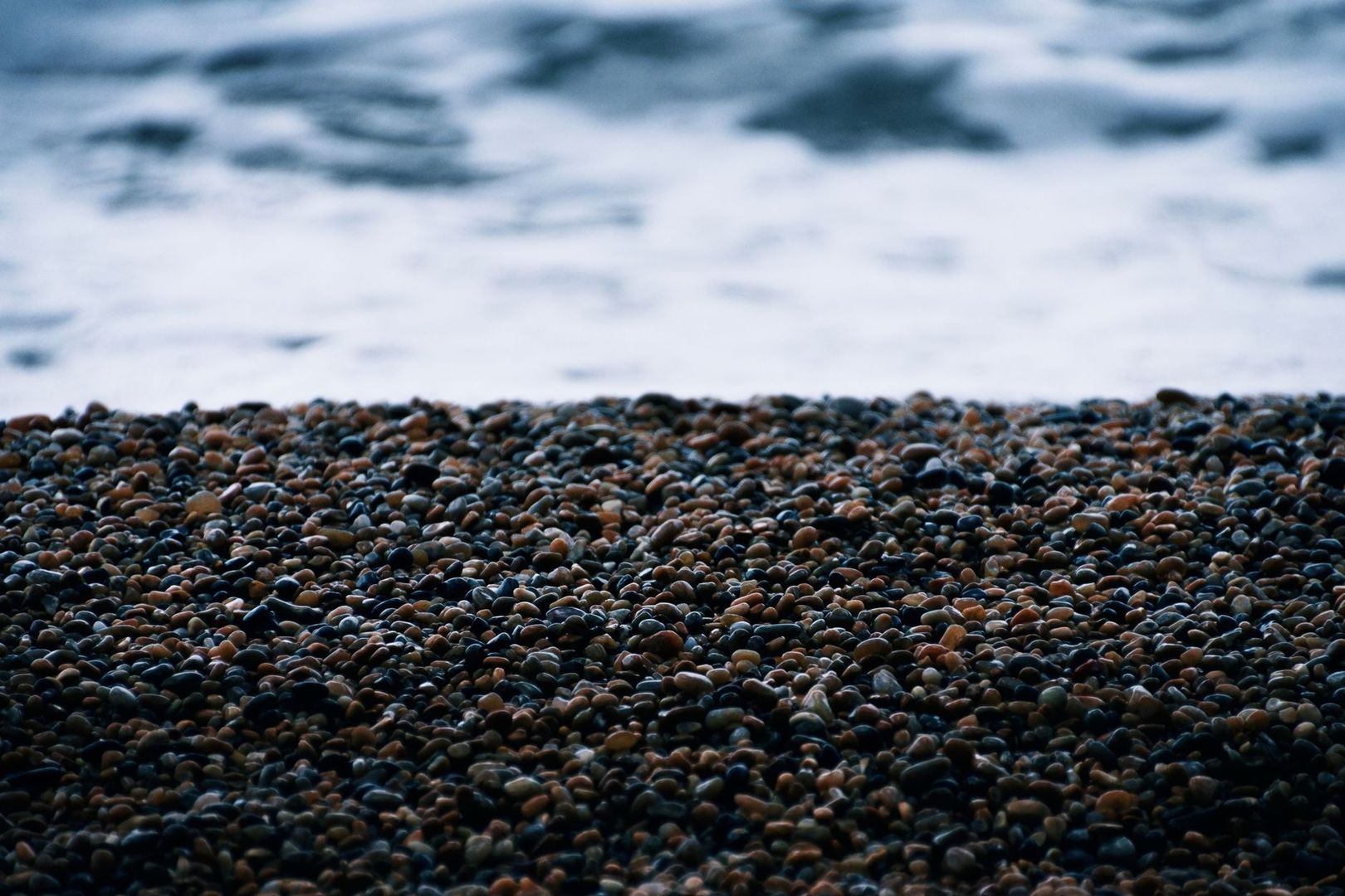 Close view of rounded shingle stones beside blurred coastal surf